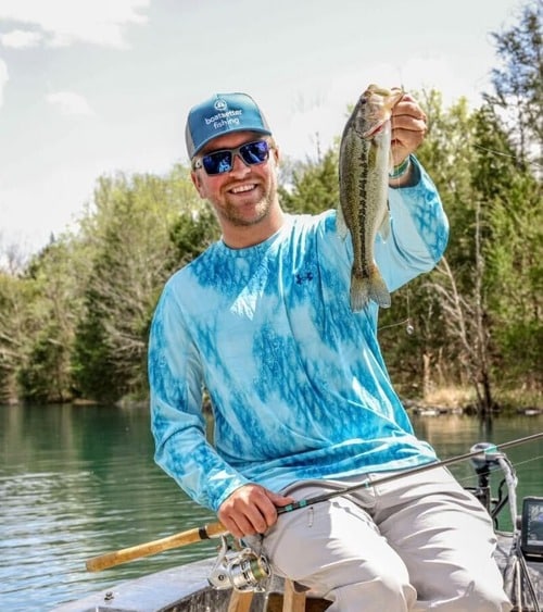 Tyler Brick holds a bass he caught fishing from a boat on a lake.