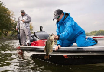 Fisher holding a bass while fishing in the rain with rain gear