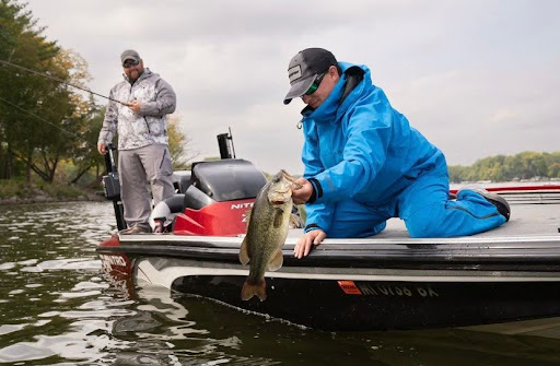 Fisher holding a bass while fishing in the rain with rain gear