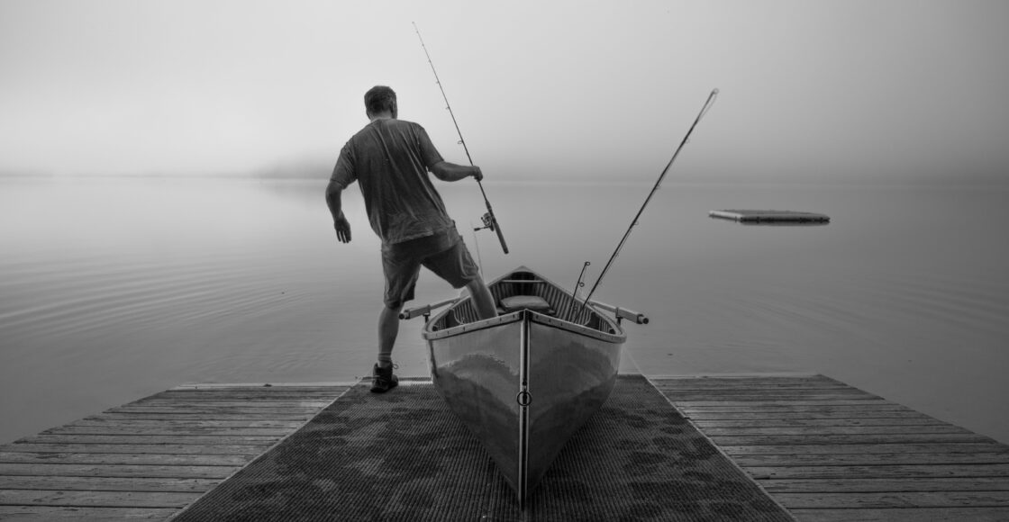 Angler stepping out of a small wooden fishing boat with rod in hand