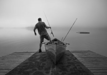 Angler stepping out of a small wooden fishing boat with rod in hand