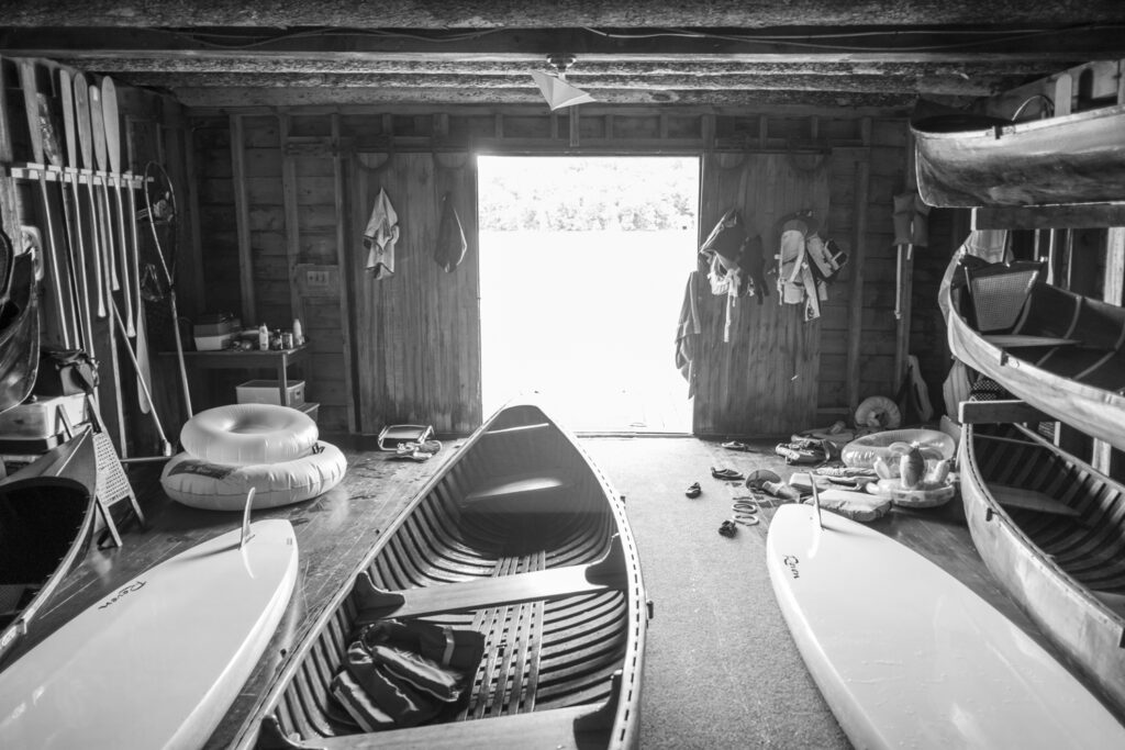 Wooden canoes, boats, surfboards, oars, and other boating gear in an large outdoorsy, wooden boat shed