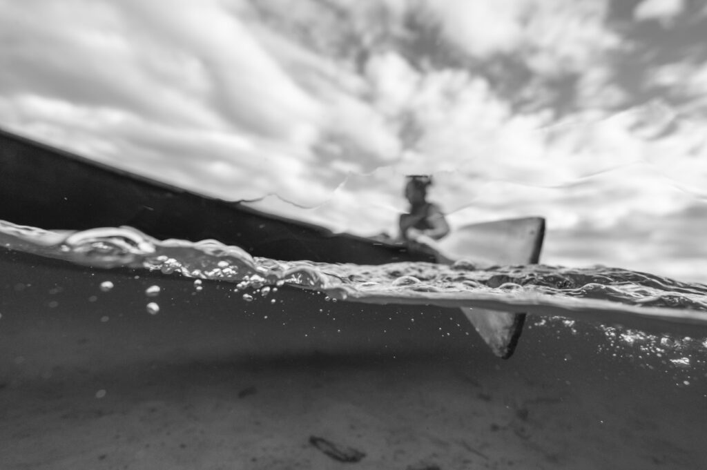 Black and white photo taken halfway underwater of a boater rowing a wooden oar