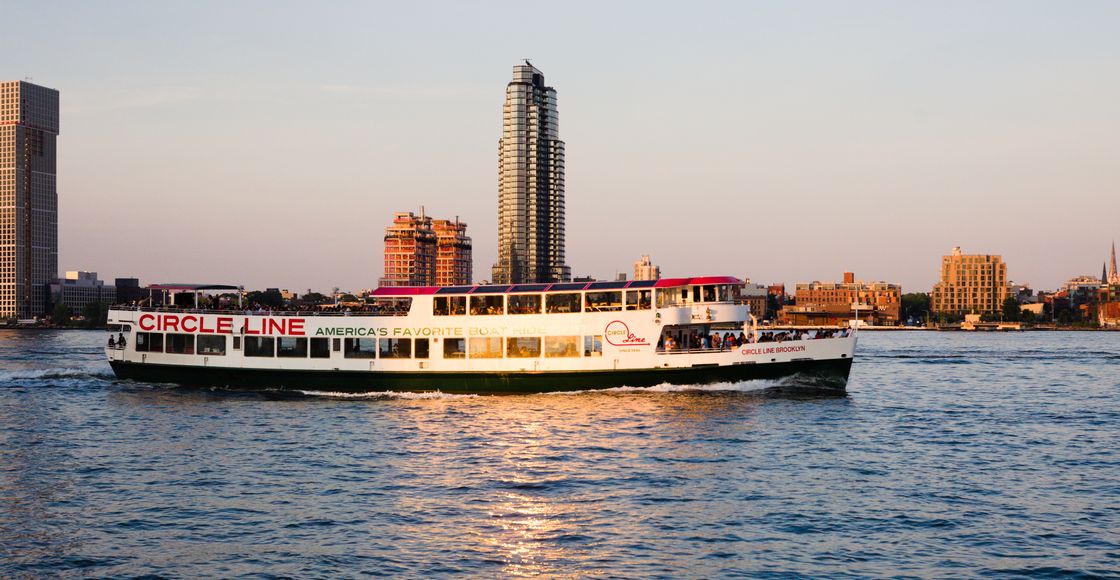 Circle Line ferry cruising in front of New York City skyline during sunset.