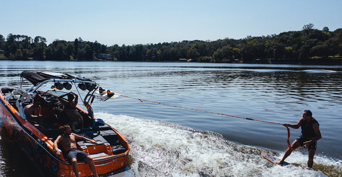 Anonymous male traveler on wake board holding rope of motor boat on foamy river while practicing extreme sport