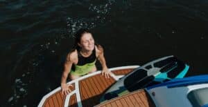 A woman in swimwear smiles joyfully while enjoying wakesurfing on a sunny day.