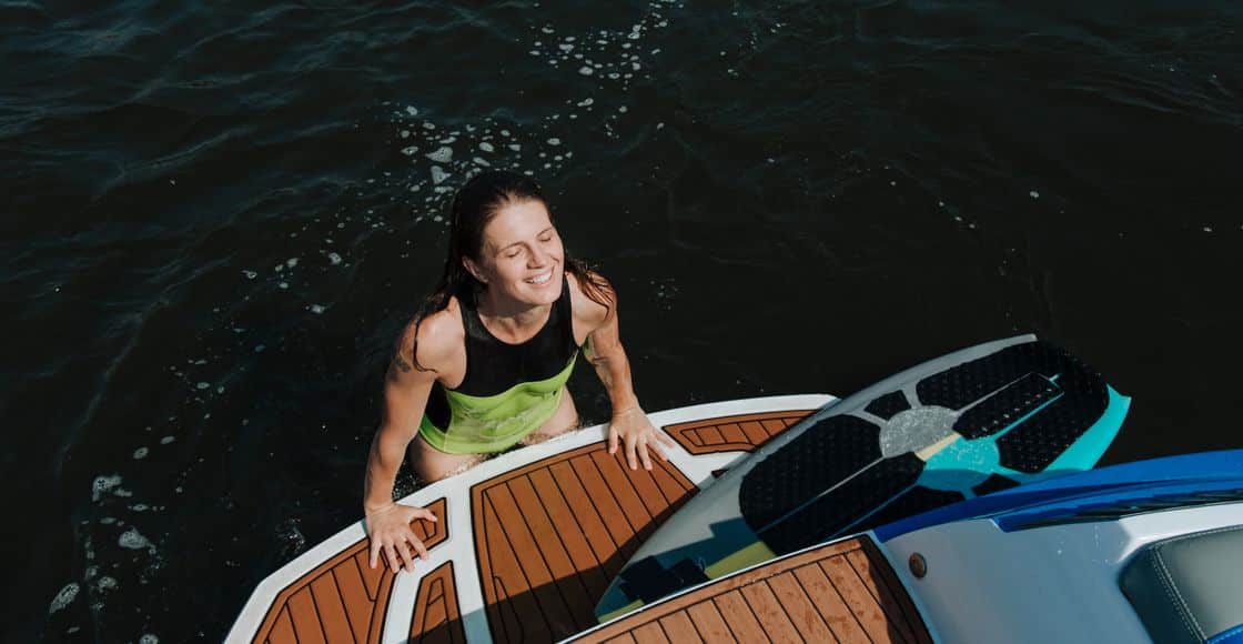 A woman in swimwear smiles joyfully while enjoying wakesurfing on a sunny day.