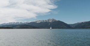 A sailboat on a serene lake against majestic mountains and a clear blue sky.