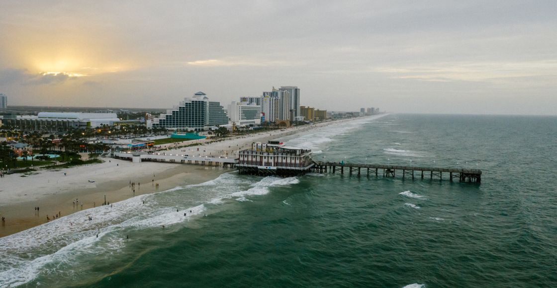 A stunning aerial view of Daytona Beach's pier and coastline at sunset with vibrant ocean waves.