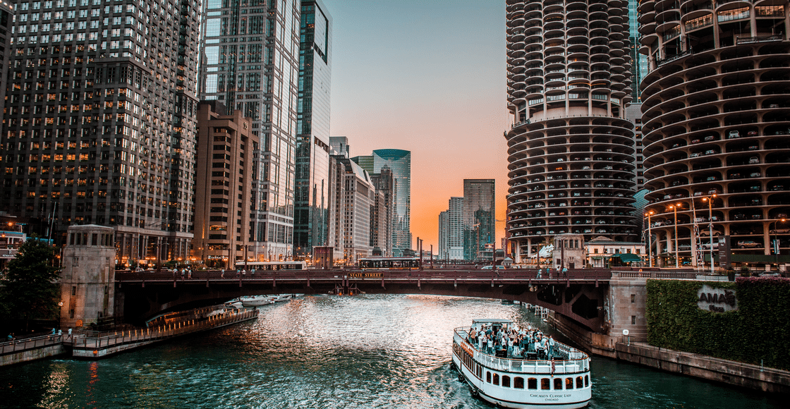 A mesmerizing view of the Chicago River with skyscrapers and a boat during sunset.