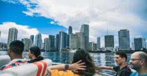 Group enjoying a boat ride with stunning view of city skyline under a bright sky.