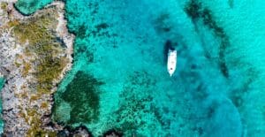Aerial shot of a boat floating in the turquoise waters of the Bahamas, showcasing vibrant coral reefs.