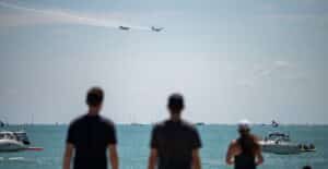 Spectators watch airplanes perform over Lake Michigan, with boats in view.
