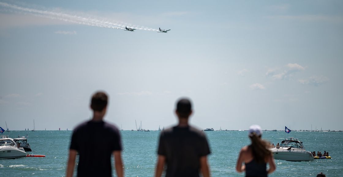 Spectators watch airplanes perform over Lake Michigan, with boats in view.
