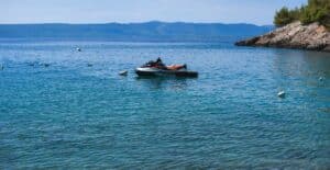 Relaxing coastal view of a jet ski on calm blue waters near a rocky coastline.