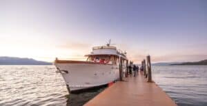 A beautiful yacht docked at a wooden pier during sunset, with serene water views and distant mountains.