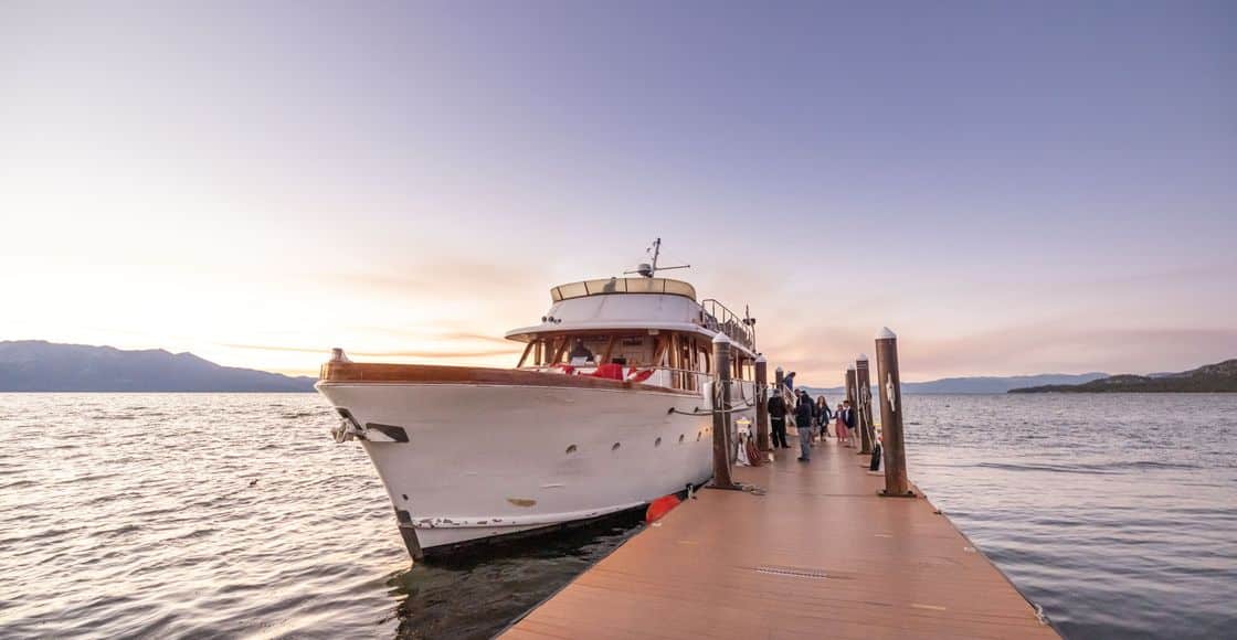 A beautiful yacht docked at a wooden pier during sunset, with serene water views and distant mountains.